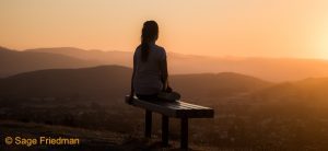Woman meditating at sunset at night looking at mountains.