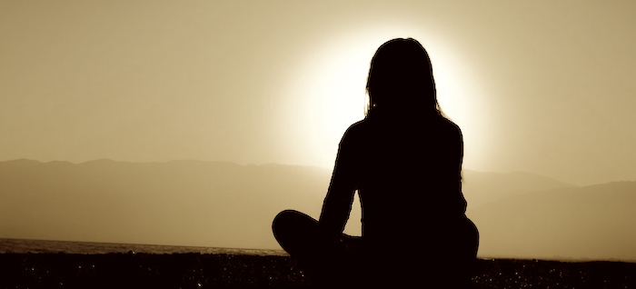 A solitary woman meditating at sunset.