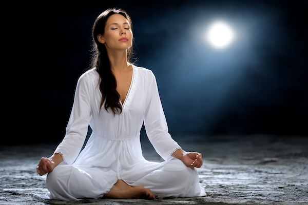 Woman meditating under moonlight.