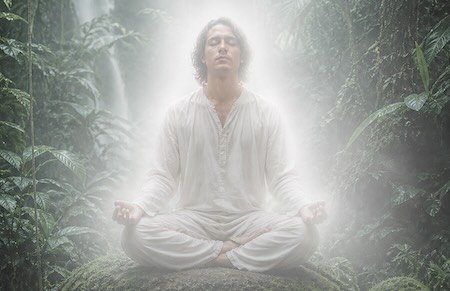Man meditating sitting on rainforest floor amidst trees and waterfall in white aura.